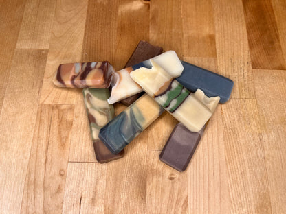 Several hand-cut soap bars with varied natural color patterns scattered on a wooden surface.