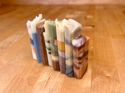 “A row of handmade soap bars standing upright on a wooden surface, each with layered natural colors and swirled patterns.”