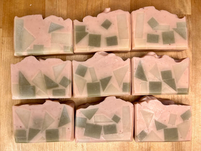 Nine Mosaic Meadow soap bars with a pale pink base and embedded green geometric soap pieces, arranged neatly on a wooden surface