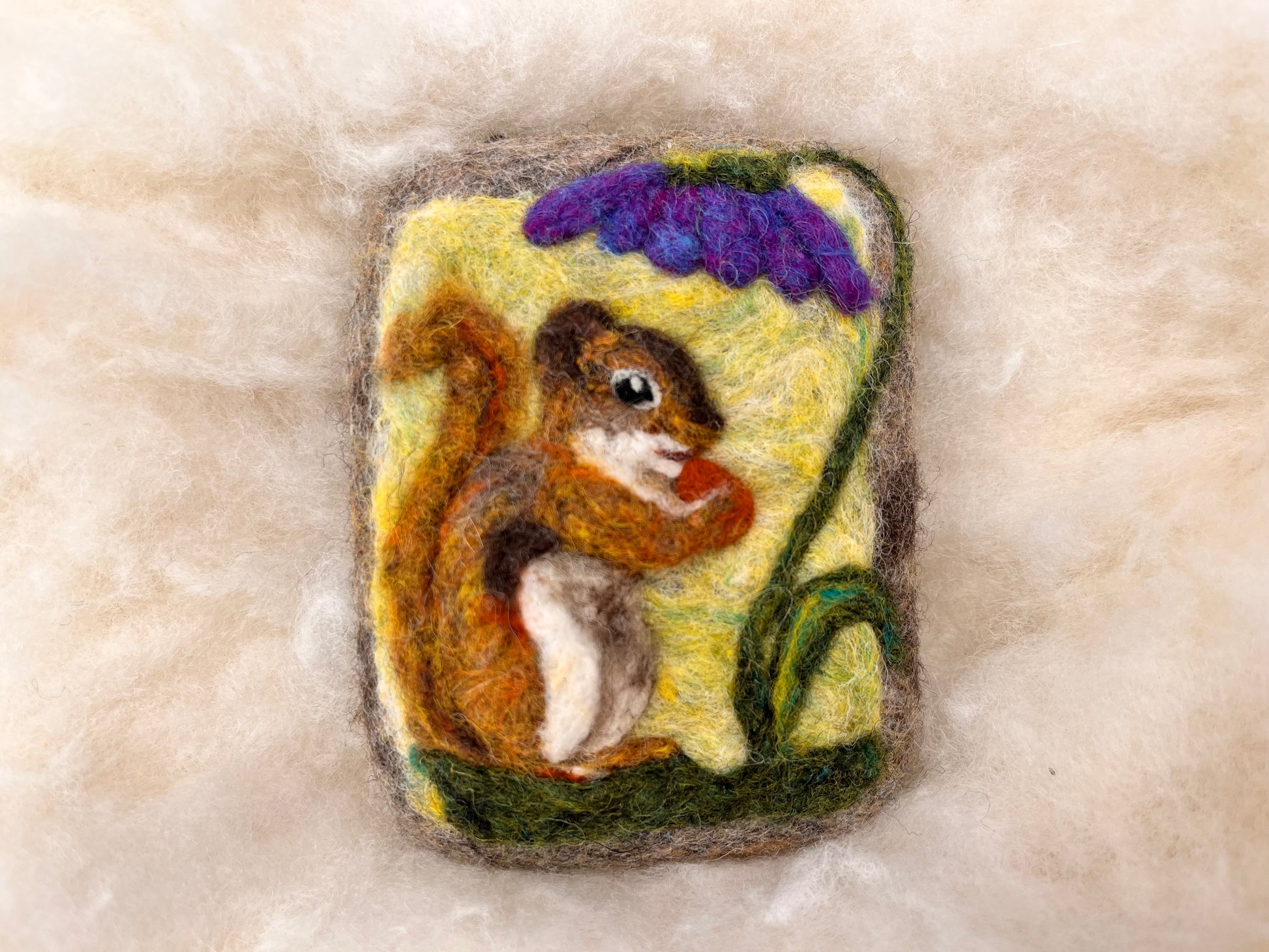 Angled view of a needle-felted red squirrel Wooly Washer with curled tail and acorn, surrounded by soft wool fibers