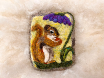 Angled view of a needle-felted red squirrel Wooly Washer with curled tail and acorn, surrounded by soft wool fibers
