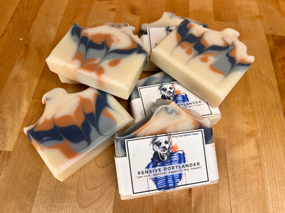 Several Pensive Portlander soap bars stacked casually on a wooden surface, highlighting their smooth sides and marbled swirl tops.