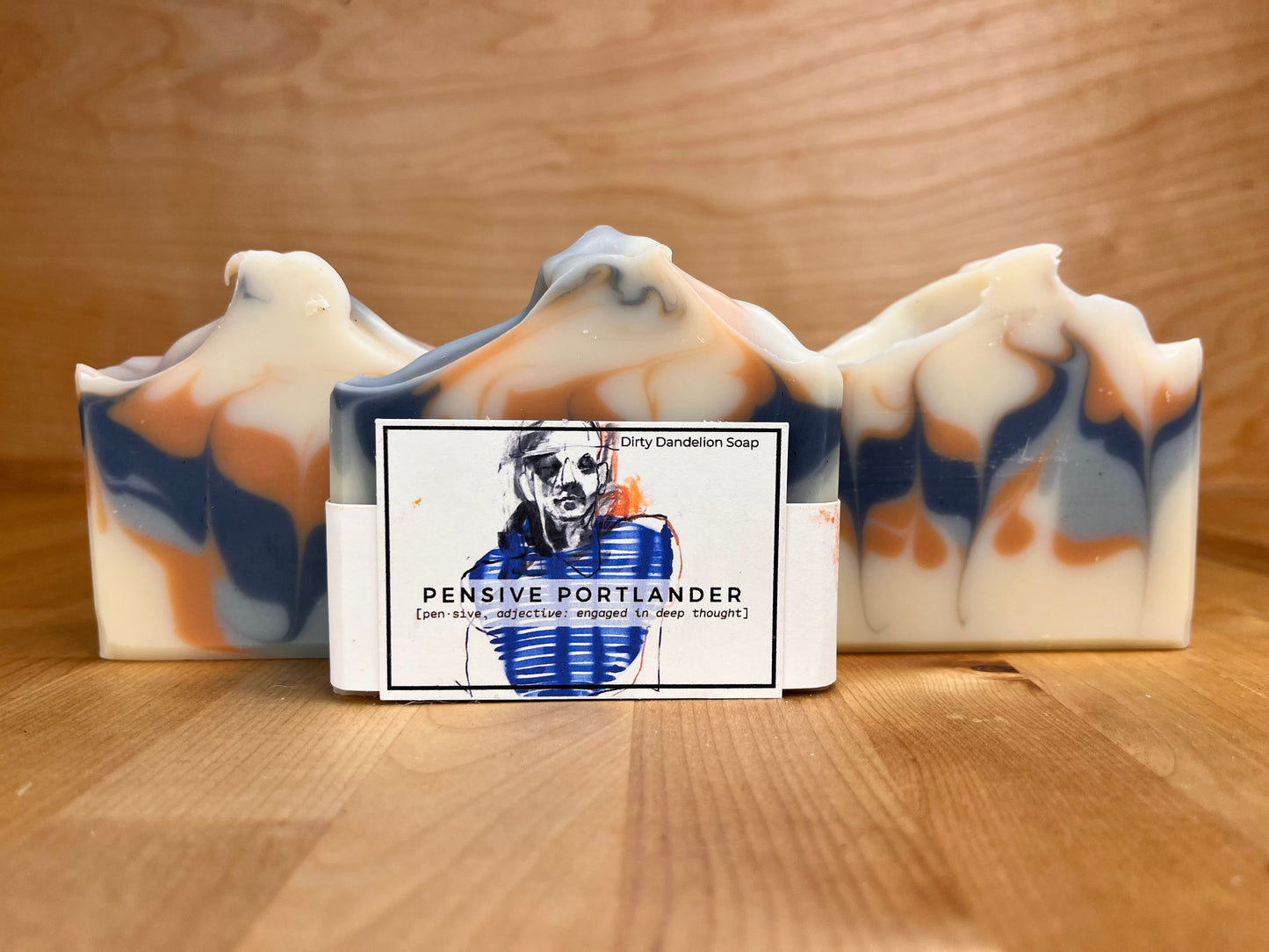 Three Pensive Portlander soap bars standing upright, with the center bar wrapped and labeled, showing blue and clay-toned swirls.
