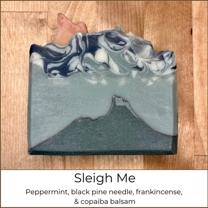 Handmade cold process soap bar with layered blue and gray swirls forming a mountain landscape design, scented with peppermint, black pine needle, frankincense, and copaiba balsam.