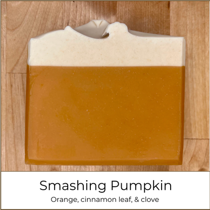 Handmade Smashing Pumpkin cold process soap bar with a warm orange base and creamy white top, photographed on a wooden surface with the scent name and essential oil blend shown below