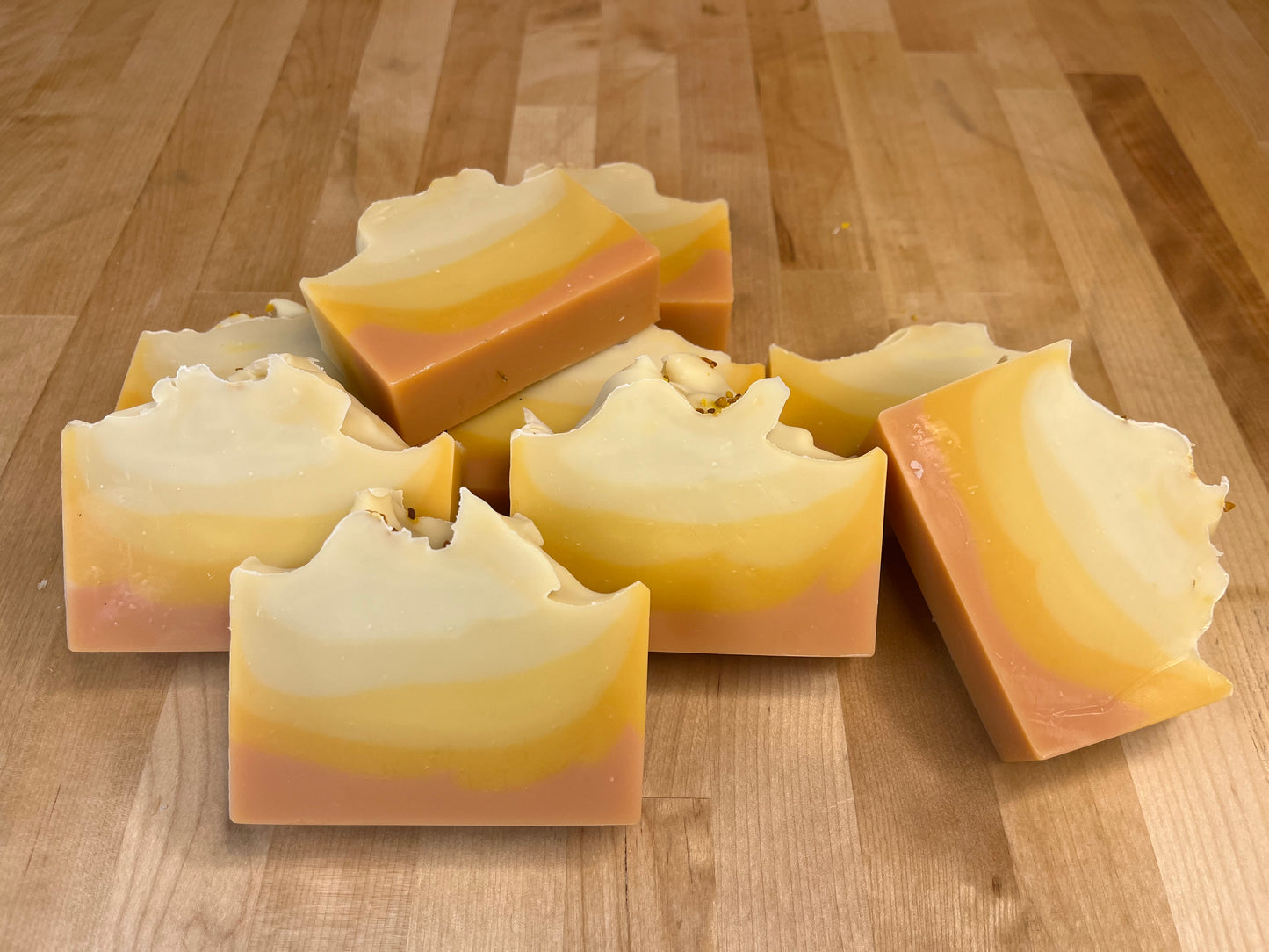 Sunrise Lift soap bars stacked and angled on a wooden surface, showing smooth curved layers of cream, pale yellow, golden orange, and blush pink with softly sculpted tops