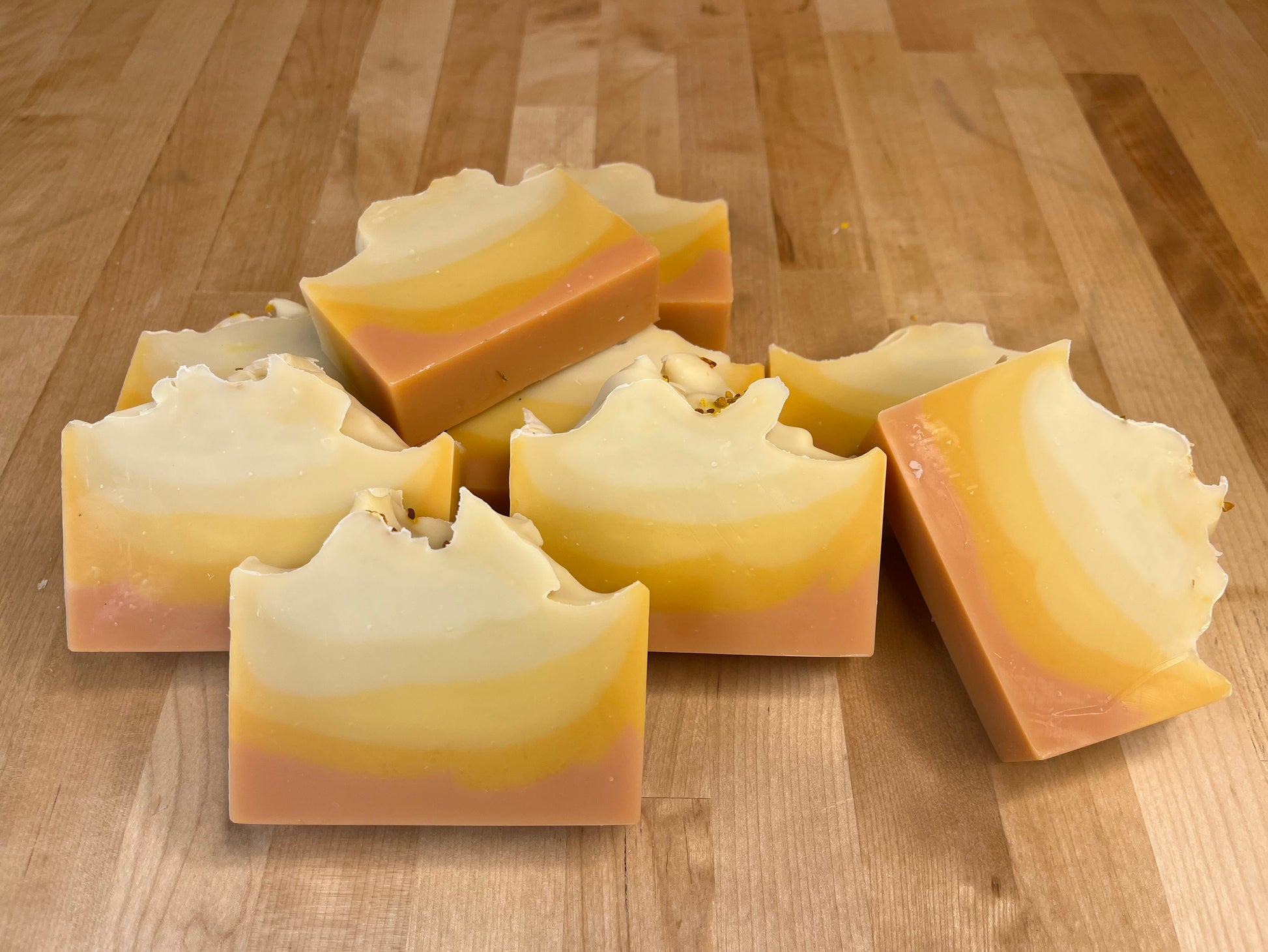 Sunrise Lift soap bars stacked and angled on a wooden surface, showing smooth curved layers of cream, pale yellow, golden orange, and blush pink with softly sculpted tops